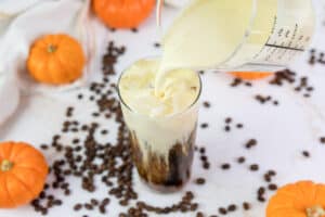 pouring pumpkin cream into a glass with cold brew coffee.