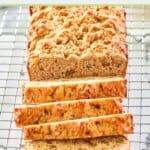 whole wheat banana nut bread loaf partially sliced on a wire rack.