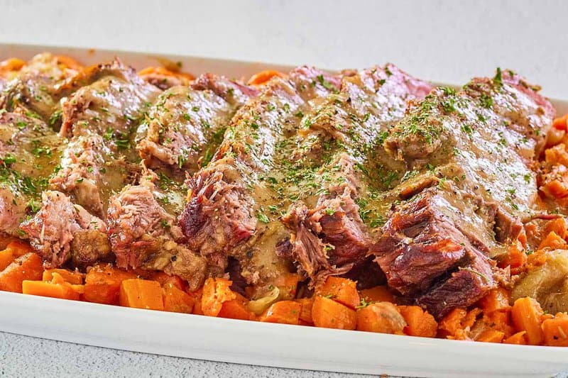 Yankee pot roast slices with gravy and vegetables on a white platter.