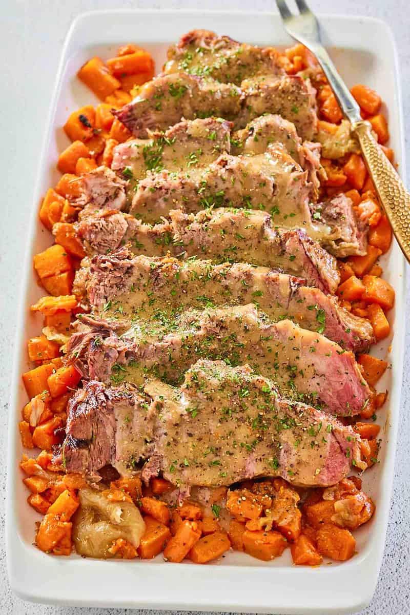 sliced Yankee pot roast with gravy and vegetables on a platter.