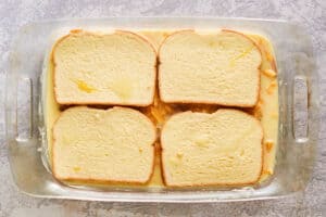 bread slices, cheese, and strata sauce in a baking dish.