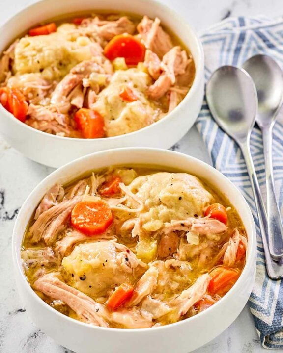 two bowls of homemade chicken and dumplings and two spoons.