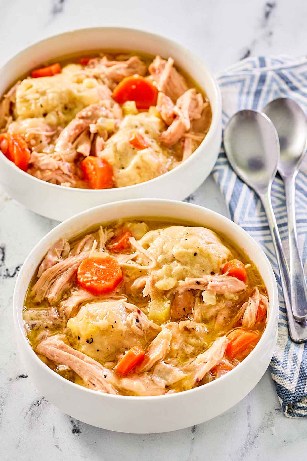 two bowls of homemade chicken and dumplings and two spoons.