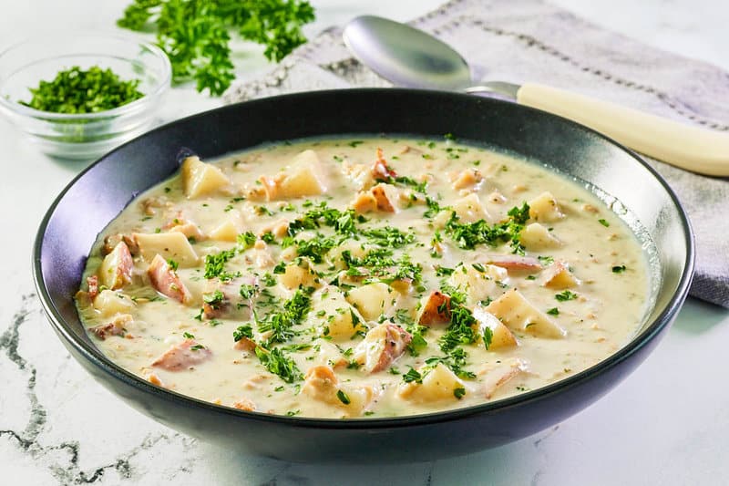 clam chowder topped with fresh parsley in a black bowl.