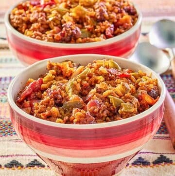 two bowls of Mexican rice casserole and spoons next to them.