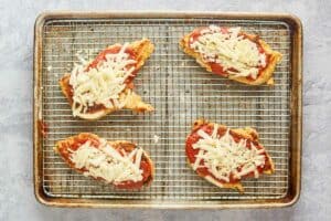 fried breaded chicken cutlets topped with marinara and cheese on a wire rack.