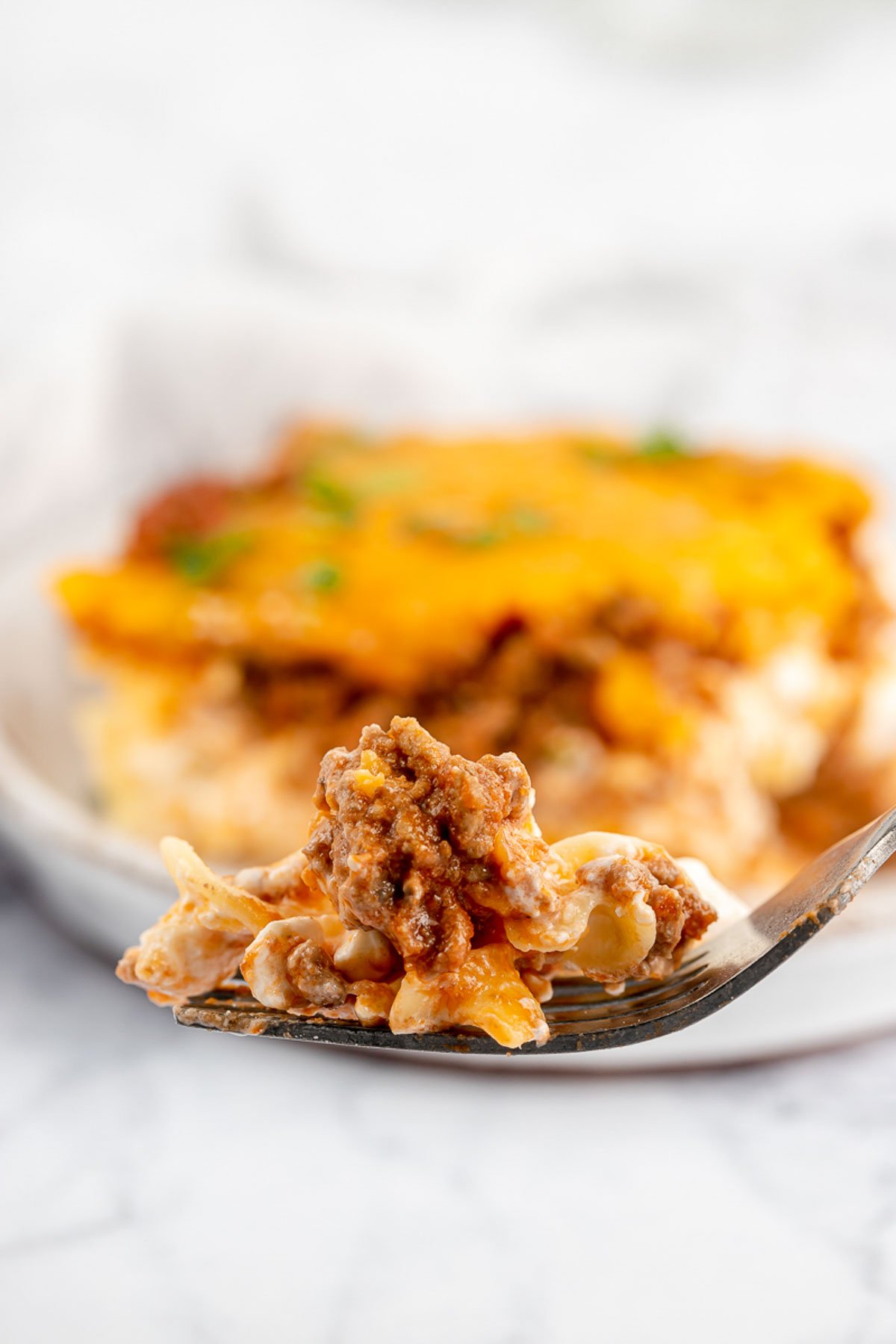 sour cream noodle bake on a fork in front of a serving on a plate.