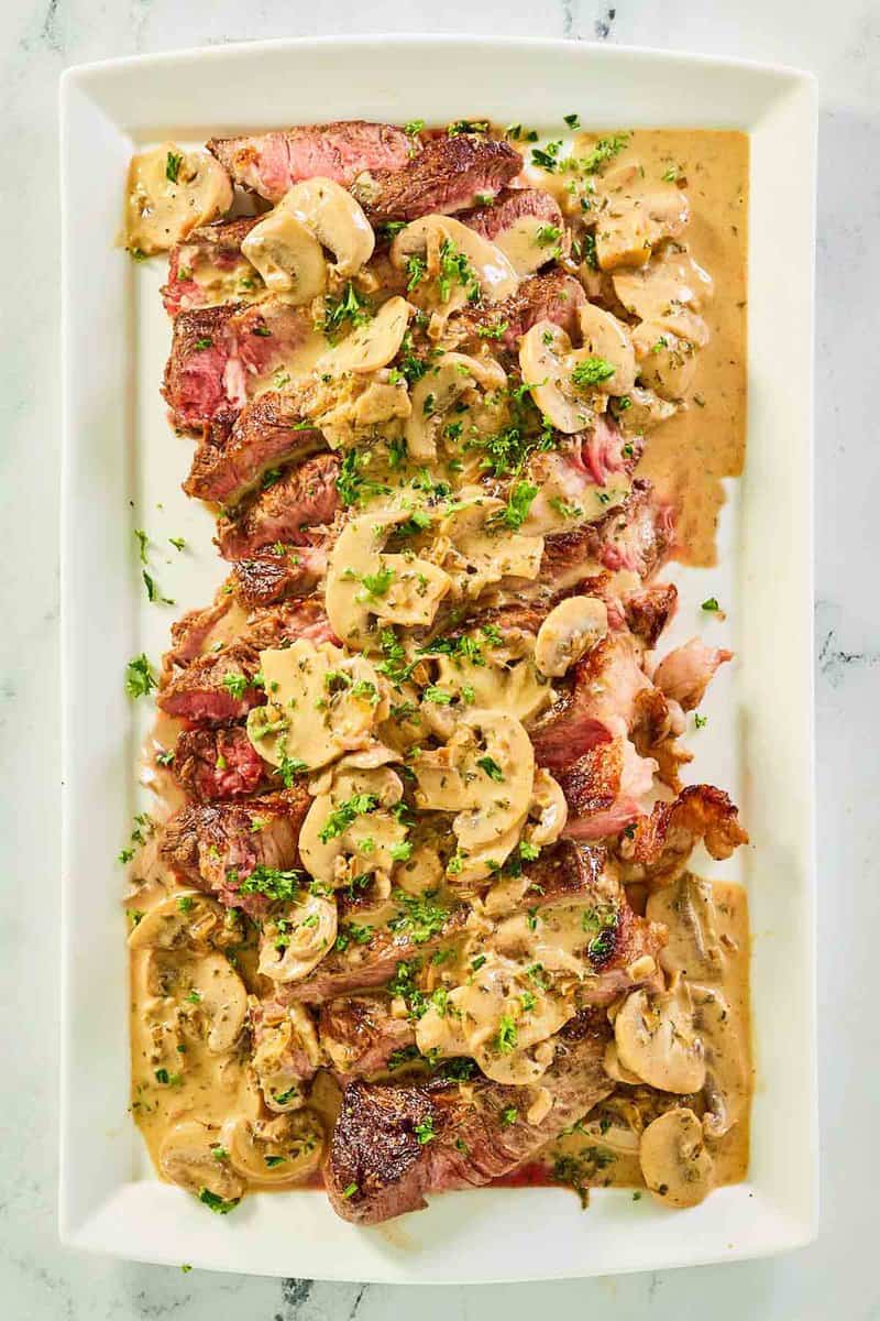 overhead view of steak marsala and sauce on a white platter.