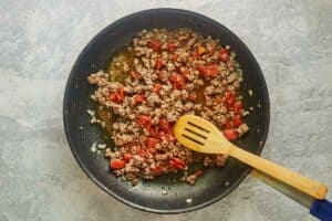 browned ground beef, onions, and tomatoes in a skillet.