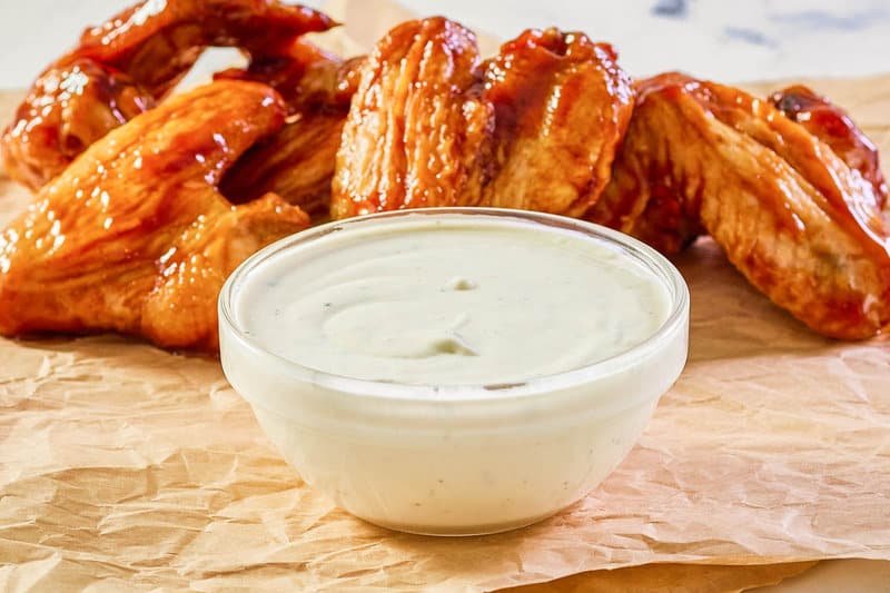 small bowl of copycat Wingstop ranch with buffalo wings behind it.