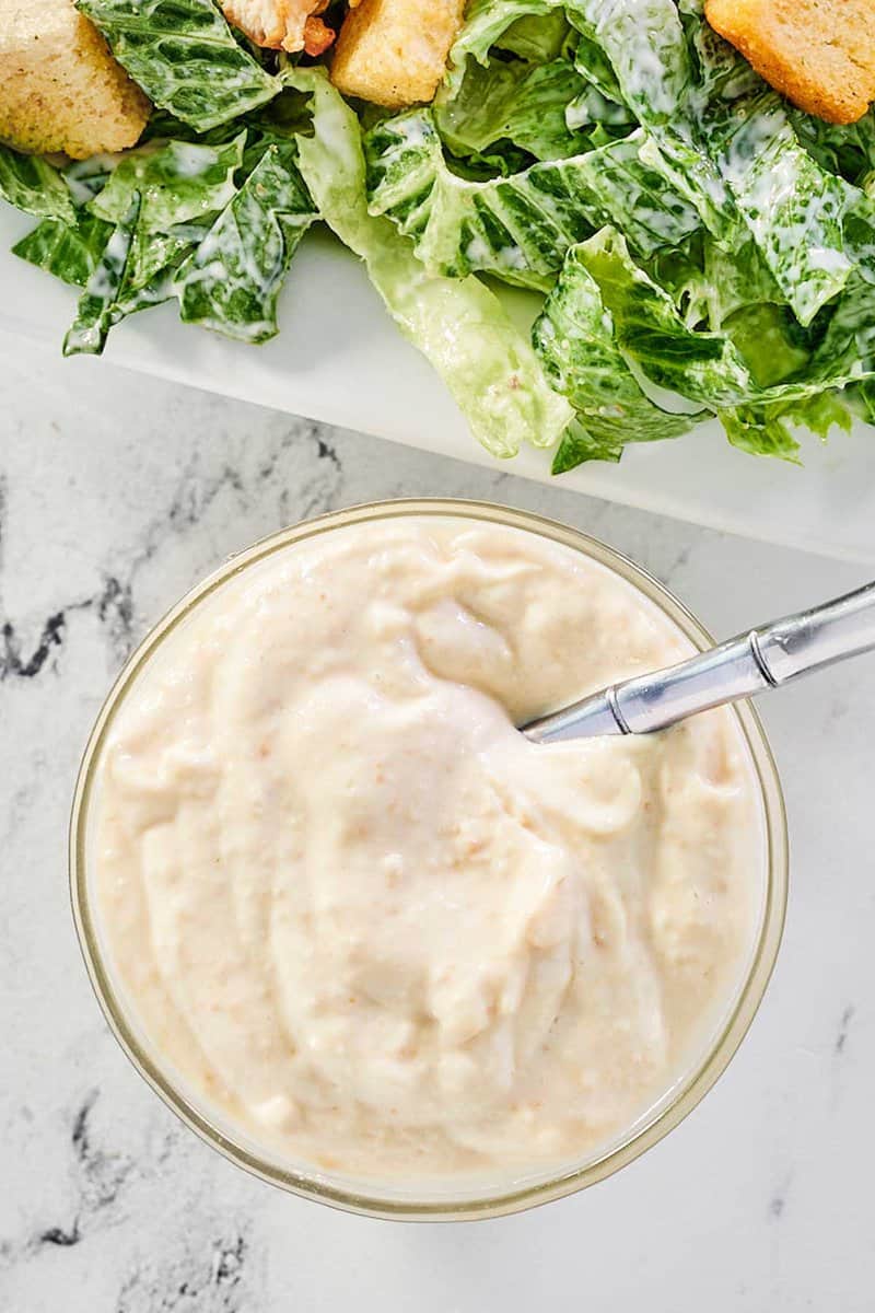 overhead view of creamy caesar dressing in a small bowl and a salad.