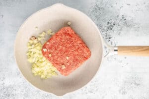 raw ground beef and chopped onions in a skillet.
