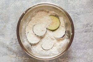 eggplant slices and seasoned flour in a bowl.