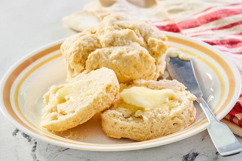 two sweet biscuits on a plate and one cut in half with butter.