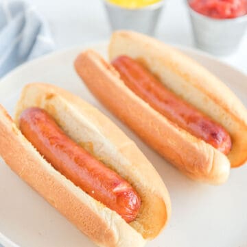 Two air fried hot dogs in buns on a plate.