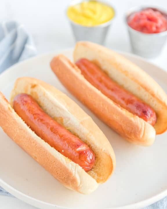 Two air fried hot dogs in buns on a plate.