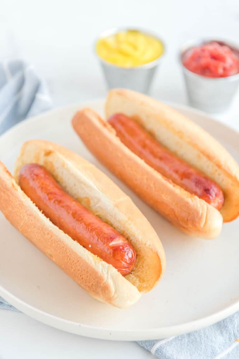 Two air fried hot dogs in buns on a plate.