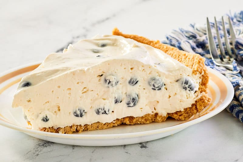 blueberry cream pie slice on a plate and a fork on a napkin.