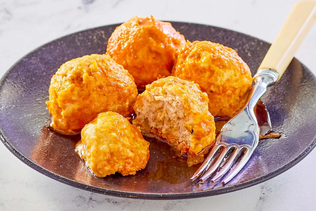 four Buffalo chicken meatballs and a fork on a black plate.