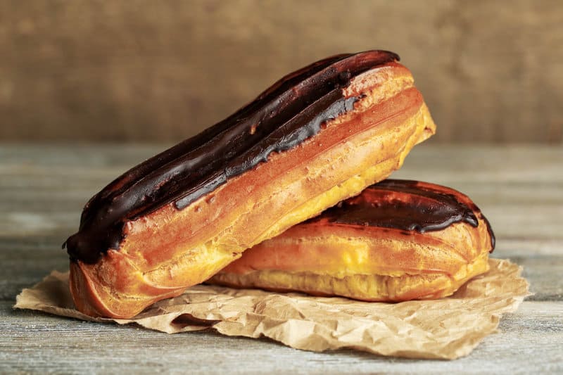 two chocolate eclairs on brown parchment paper.