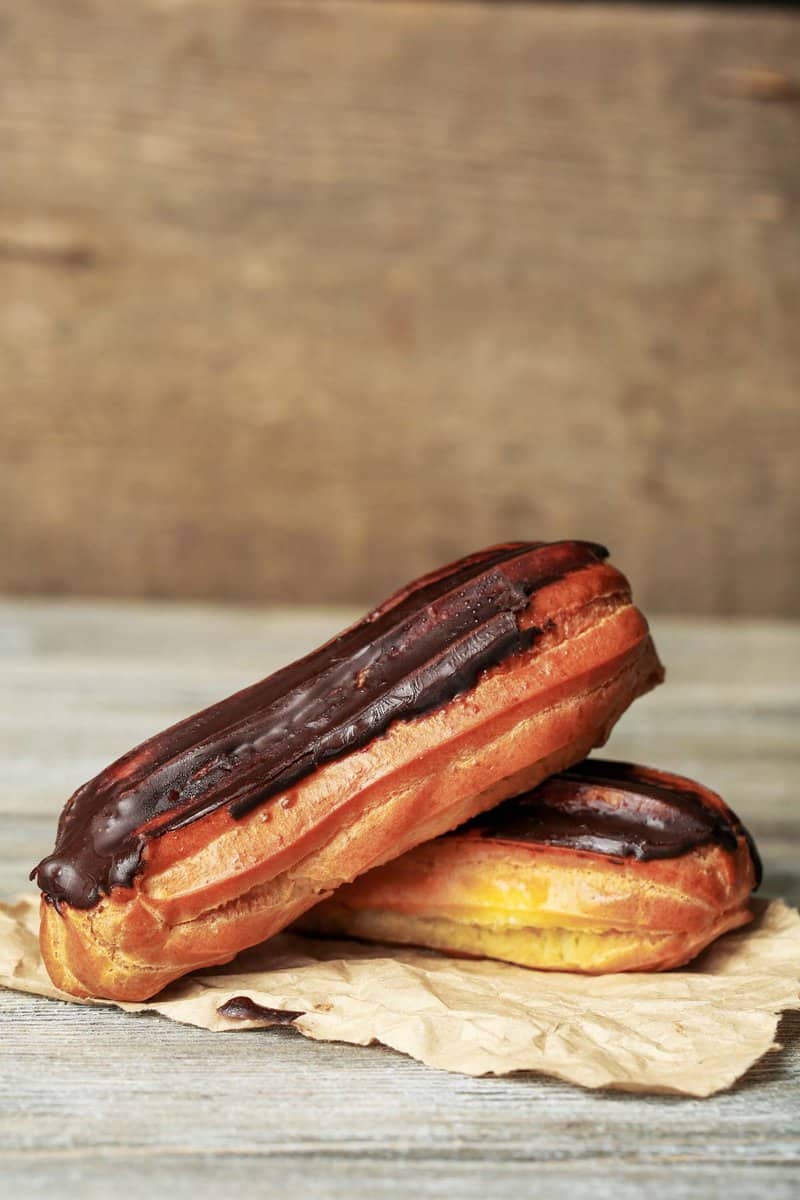two homemade chocolate eclairs on brown parchment paper.