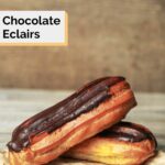 two chocolate eclairs on parchment paper.