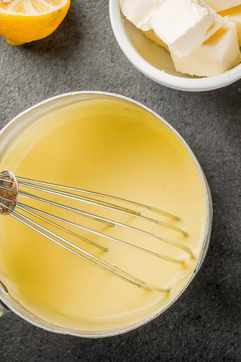 overhead view of homemade hollandaise sauce and a whisk in a pan.