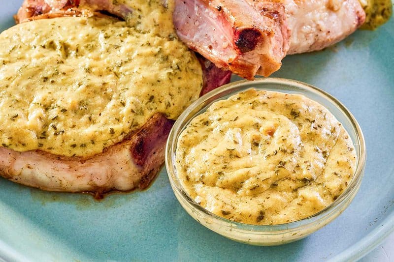 Mustard cream sauce in a small glass bowl next to pork chops with the sauce on them.