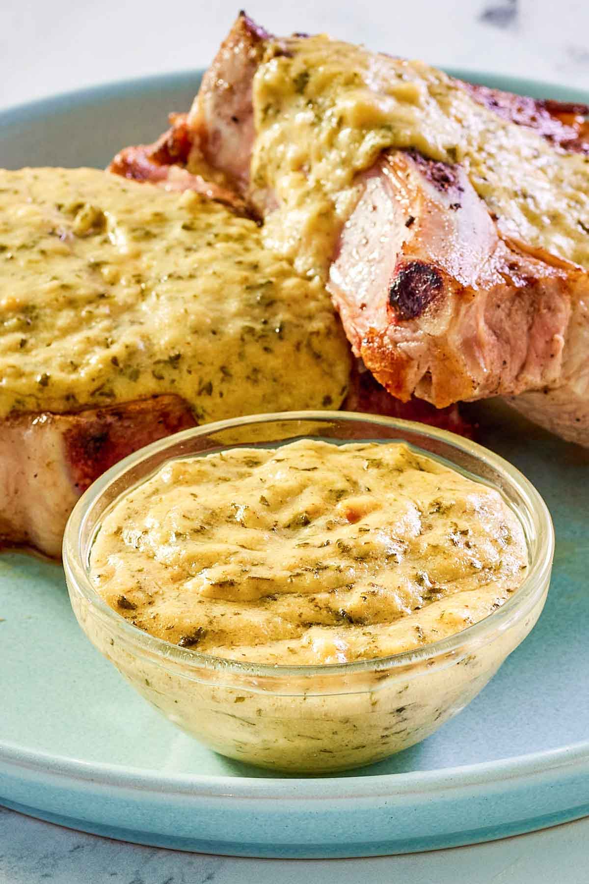 Mustard cream sauce in a small bowl and over pork chops on a plate.