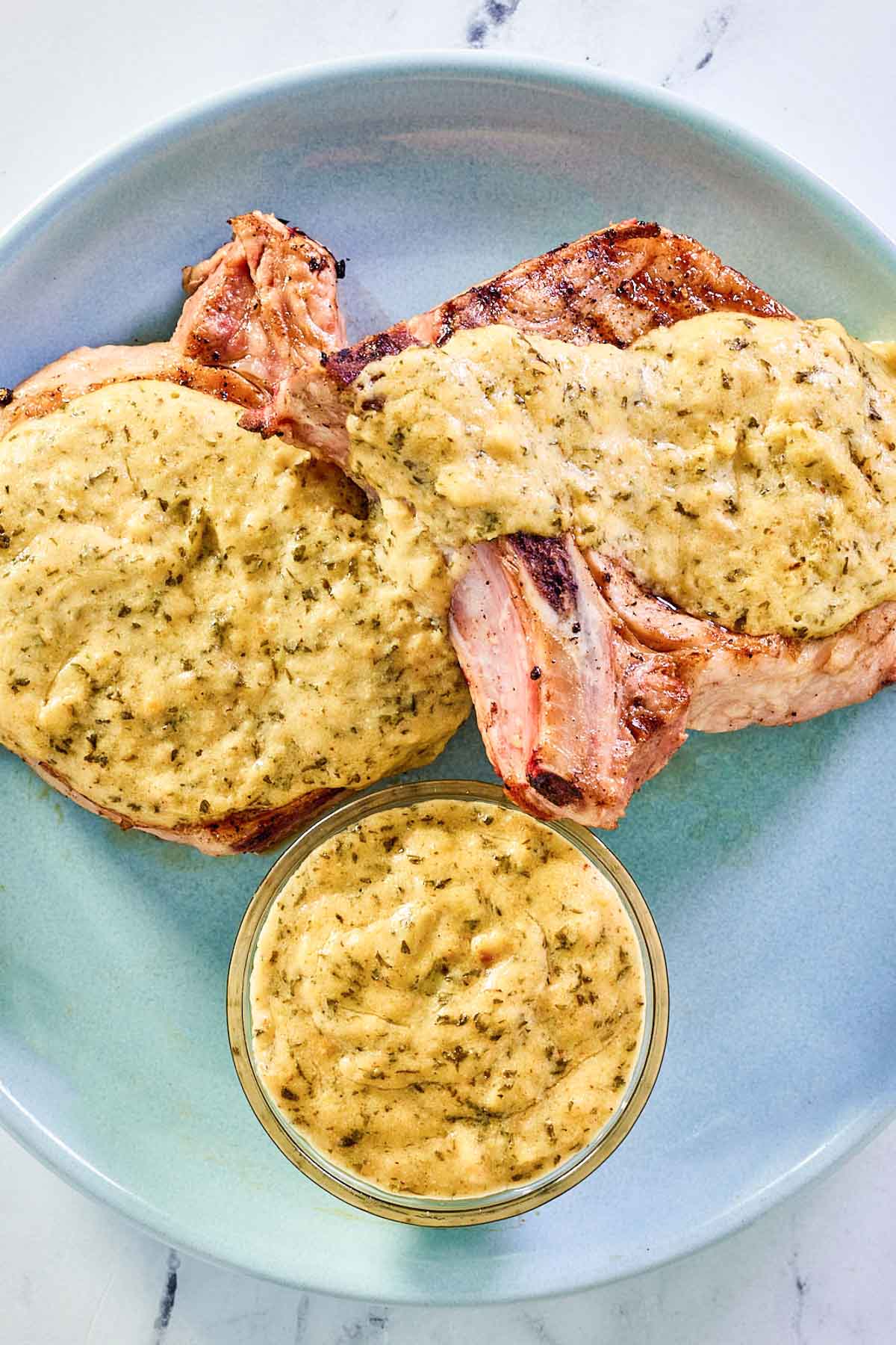overhead view of mustard cream sauce on pork chops and in a small bowl on a plate.