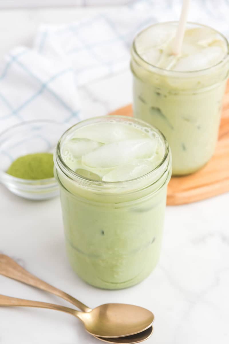 two copycat Starbucks iced matcha latte drinks and matcha powder in a bowl.