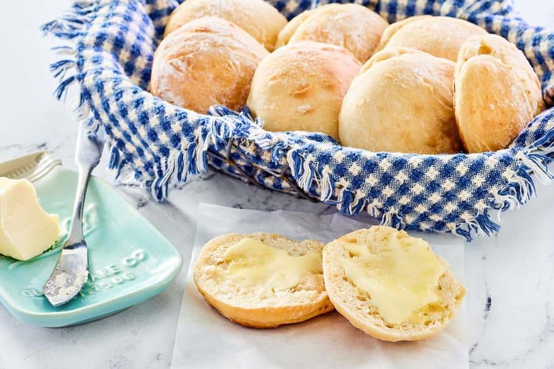 A basket of angel biscuits and one split open with butter on it.