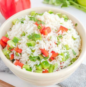 Cilantro rice with bell peppers in a bowl, a red bell pepper, and fresh cilantro.