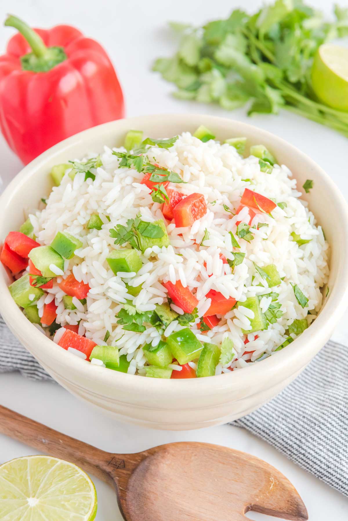 Cilantro rice with bell peppers in a bowl, a red bell pepper, and fresh cilantro.