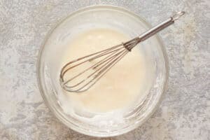 Cake glaze mixture and a whisk in a bowl.