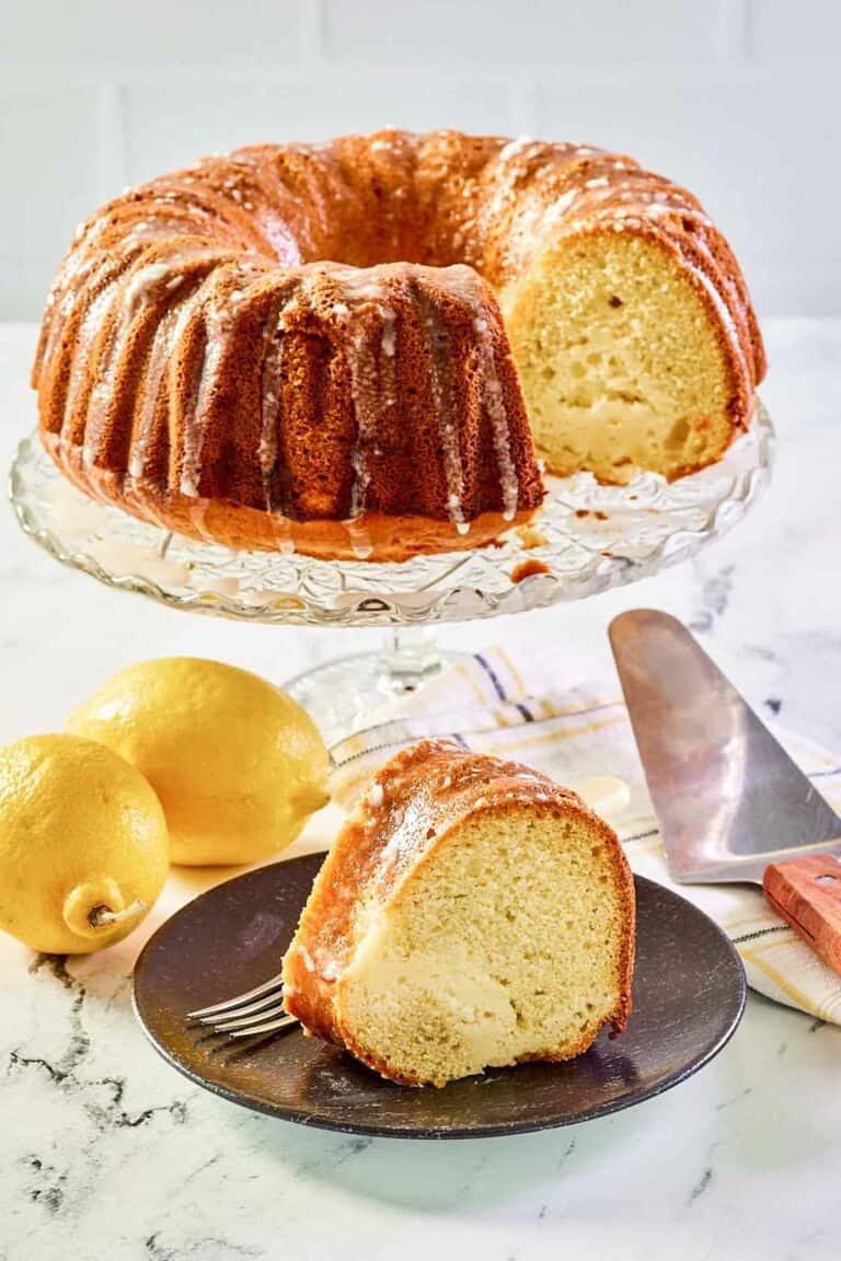 Cream cheese coffee cake on a cake stand and a slice on a plate.