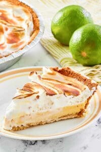 Key lime meringue pie slice on a plate and two limes.