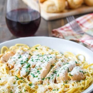 Copycat Olive Garden grilled chicken alfredo, a glass of wine, and bread.