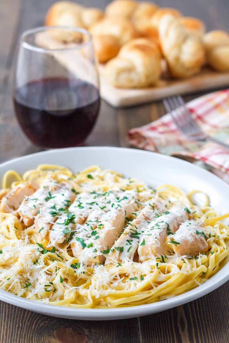 Copycat Olive Garden grilled chicken alfredo, a glass of wine, and bread.