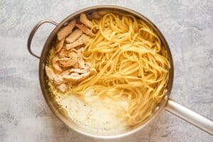 Chicken pasta, and alfredo sauce in a pot.