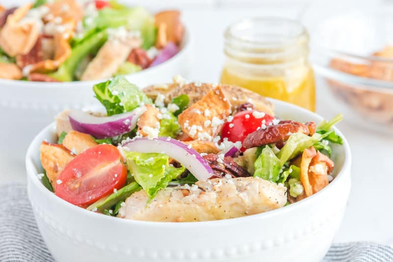 A bowl of copycat Paneral fuji apple salad and a jar of dressing behind it.