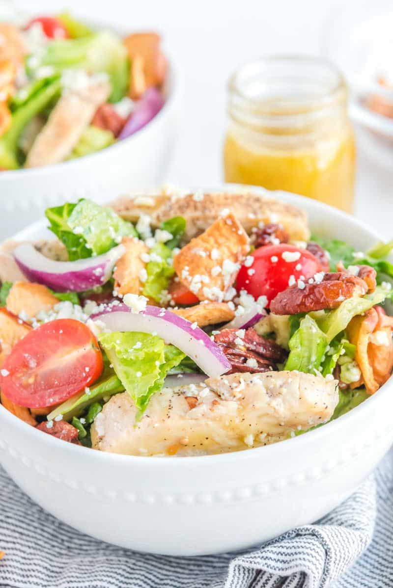 Copycat Panera fuji apple salad in a bowl and the dressing in a jar behind it.