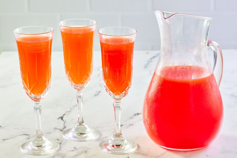 Strawberry mimosa in a pitcher and three glasses.