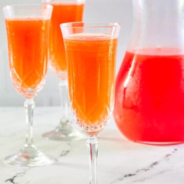 Strawberry mimosa in three glasses and a pitcher.