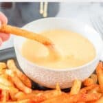 Homemade Taco Bell nacho fries and dipping one into cheese sauce.