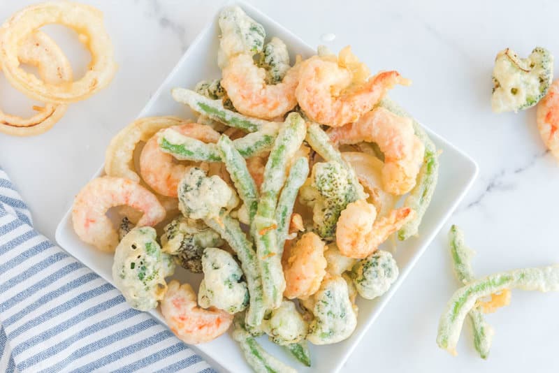 Overhead view of homemade tempura fried shrimp and veggies on a square plate.