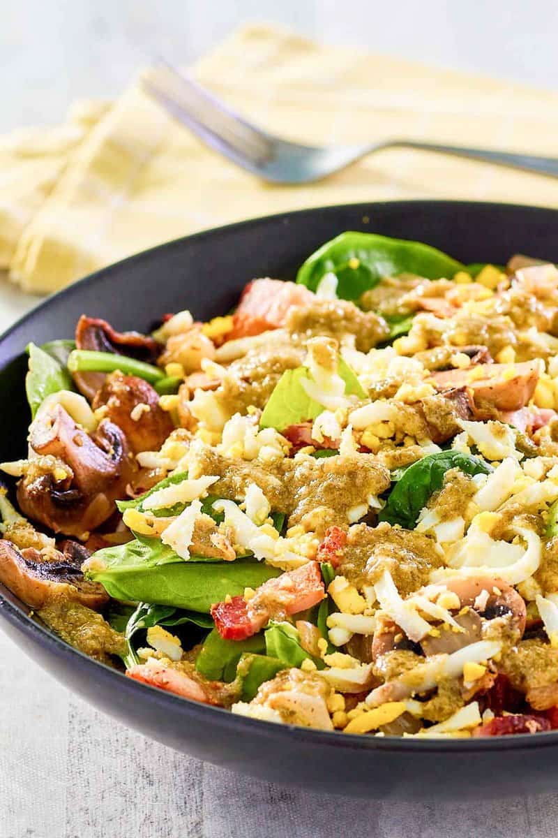 Copycat Chart House spinach salad with eggs and bacon dressing in a bowl.