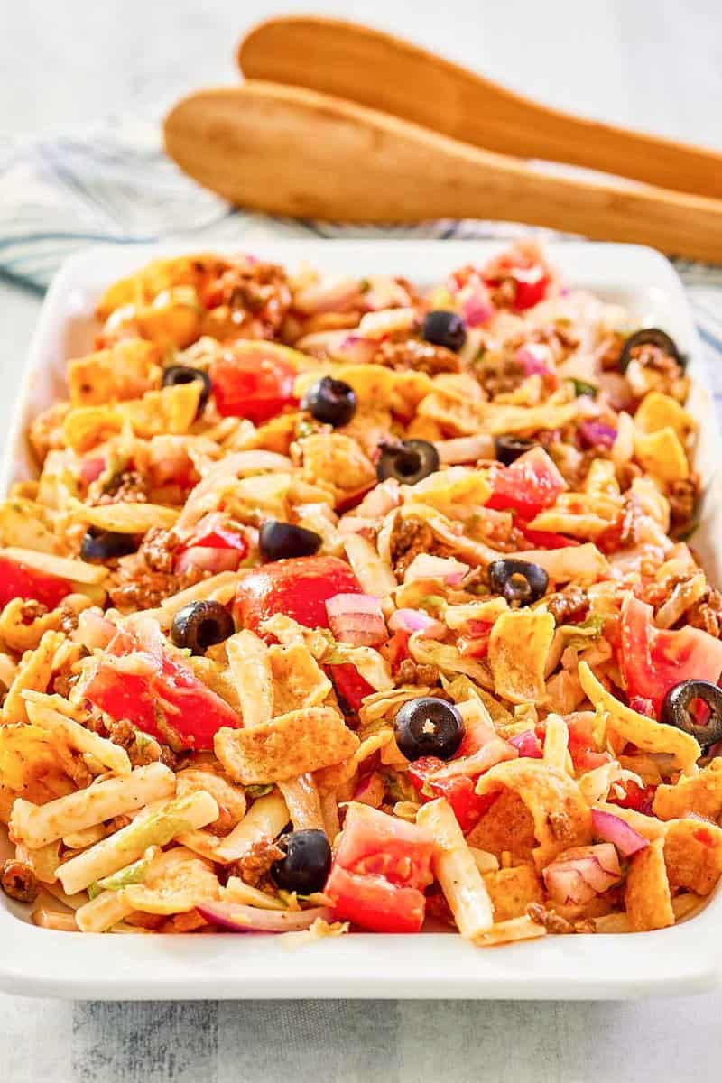 Frito taco salad on a platter and wood salad tongs.