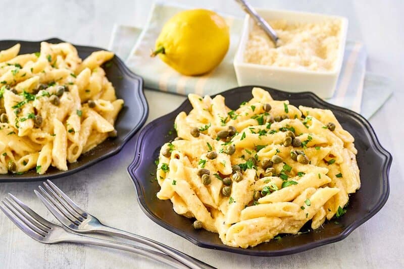 Greek pasta with citrus  alfredo sauce, a lemon, and a tiny  crockery  of parmesan cheese.