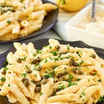 Greek pasta with lemon alfredo sauce on two plates, parmesan cheese, and a lemon.